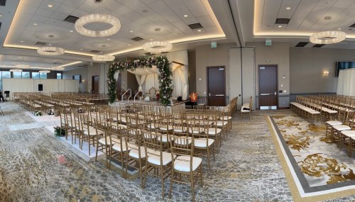 A beautifully decorated wedding venue with floral arch, rows of chairs, and elegant chandeliers.