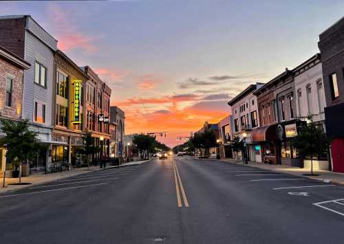 A quiet street lined with shops and restaurants, illuminated by a vibrant sunset sky.