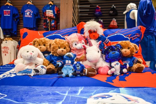 A colorful bedspread featuring plush toys, including bears, a unicorn, and a blue mascot, in a sports-themed room.