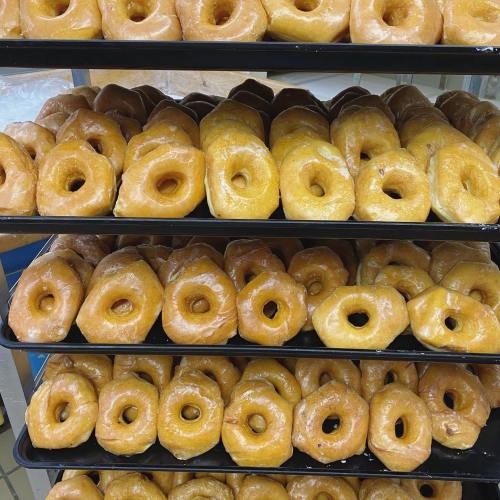 A display of freshly made, golden-brown donuts stacked on trays, showcasing their round shapes and glazed surfaces.
