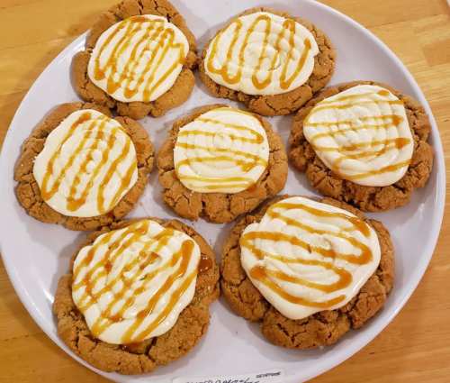 A plate of eight large cookies topped with cream and drizzled with caramel sauce.
