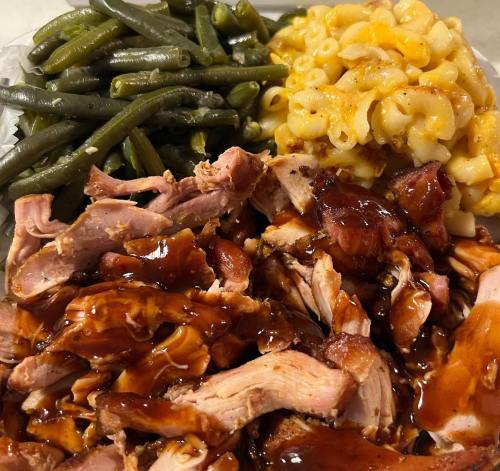 A plate featuring shredded barbecue chicken, macaroni and cheese, and green beans.