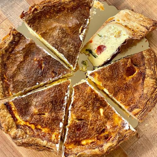A freshly baked quiche cut into slices, showcasing a golden crust and creamy filling with visible ingredients.