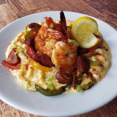 A plate of shrimp and sausage over creamy grits, garnished with lemon and green onions.