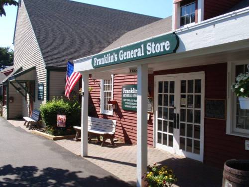 Exterior of Franklin's General Store, featuring a sign, American flag, and benches in a quaint, sunny setting.
