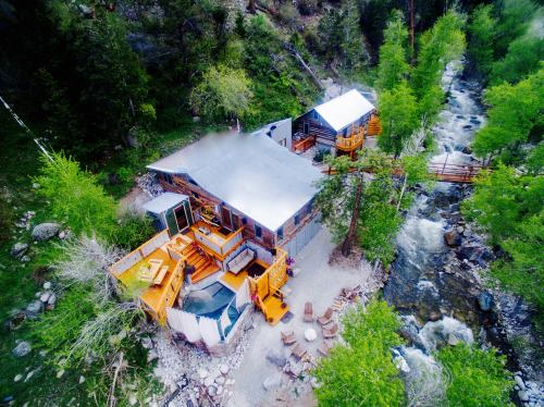 Aerial view of a rustic cabin by a river, surrounded by lush greenery and outdoor seating areas.