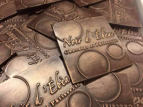 A collection of bronze-colored chocolate packaging with the text "Noir d'Ébène Chocolat et Pâtisserie" embossed on it.