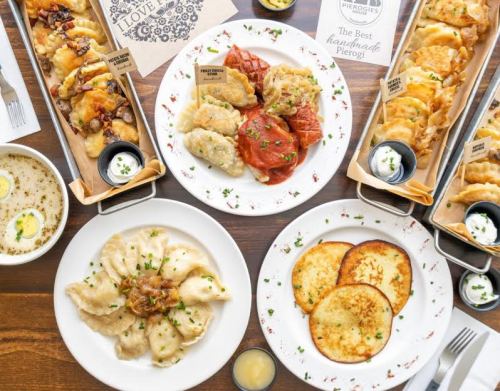 A spread of various pierogi dishes, including fried and boiled pierogi, served with sour cream and garnished with herbs.
