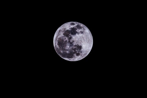 A bright full moon against a black night sky, showcasing its craters and surface details.