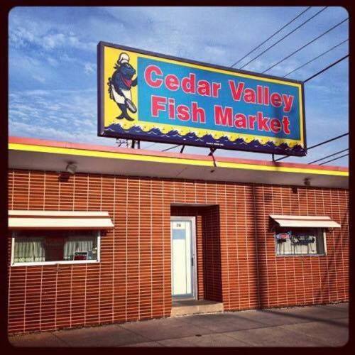 Exterior of Cedar Valley Fish Market with a colorful sign and brick facade under a blue sky.