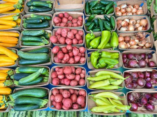 A variety of fresh vegetables in baskets, including zucchini, potatoes, peppers, and onions, arranged neatly.