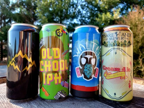 Four colorful beer cans displayed outdoors, featuring unique designs and labels from different breweries.