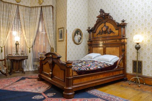 A vintage wooden bed with a patterned blanket in a room featuring ornate curtains and decorative furnishings.