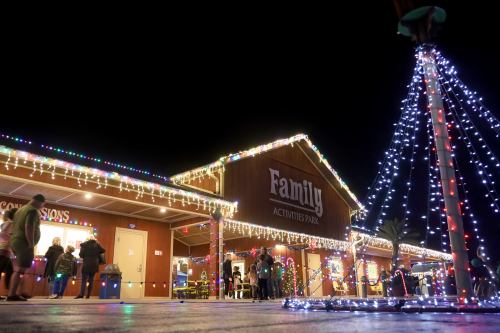 A festive family activity park adorned with colorful holiday lights at night, with people enjoying the atmosphere.