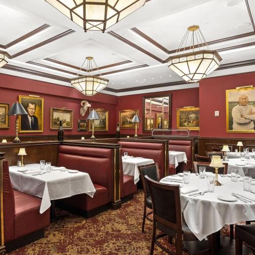 Elegant restaurant interior with red walls, white tablecloths, and vintage portraits. Cozy booths and warm lighting.