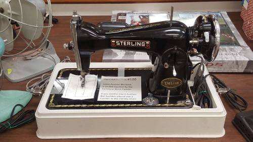 A vintage Sterling sewing machine displayed for a silent auction, with a sign detailing auction information.
