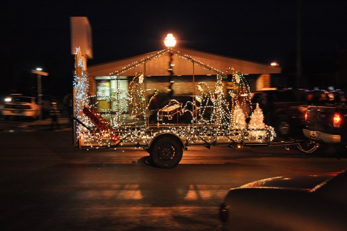 A decorated trailer with colorful lights and festive ornaments, moving past a building at night.