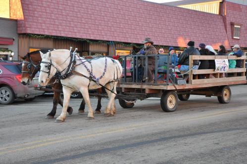 A horse-drawn wagon carries people down a street, with shops visible in the background.