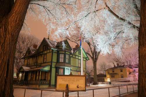 Historic mansion illuminated by winter lights, surrounded by frosted trees and a snowy landscape.