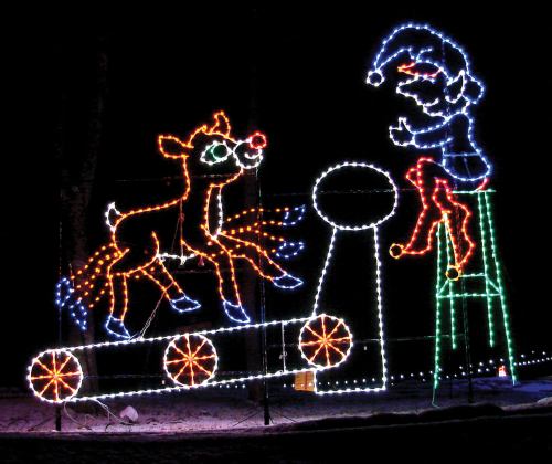 A colorful light display featuring a reindeer and an elf on a train, set against a dark background.