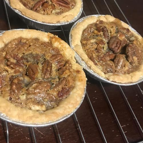 Three mini pecan pies cooling on a wire rack, with golden crusts and a rich, nutty filling topped with whole pecans.