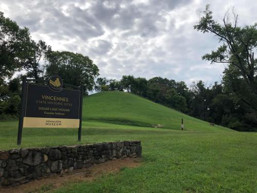 Sign for Vincennes State Historic Sites with a grassy mound and cloudy sky in the background.