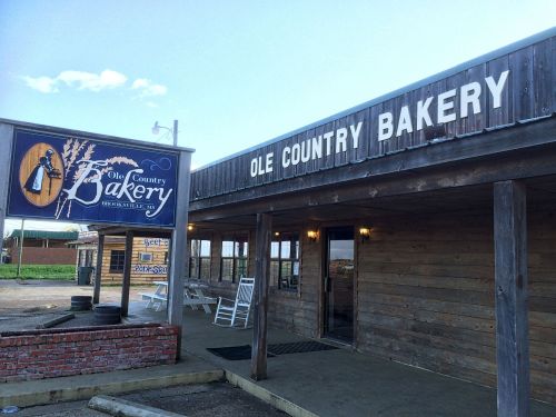 Exterior of Ole Country Bakery featuring a wooden facade and a sign with a wheat design. Clear blue sky in the background.