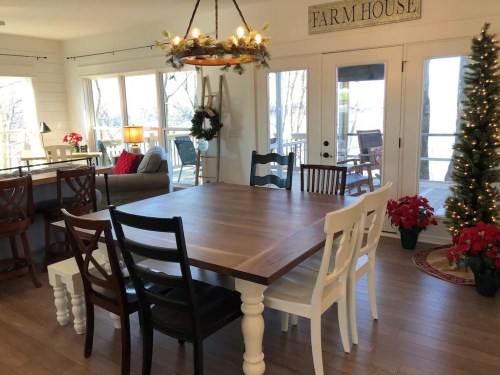 A cozy dining area with a large wooden table, mixed chairs, and festive decorations, including a Christmas tree.