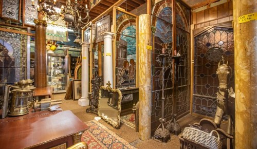 A vintage shop filled with ornate stained glass, antique furniture, and decorative items in a cozy, cluttered setting.