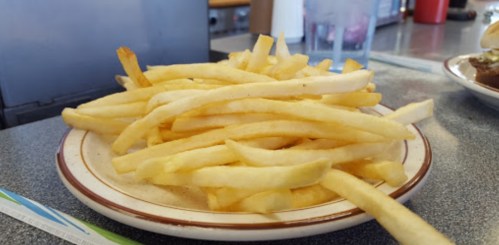 A plate of golden, crispy French fries stacked high on a diner table.