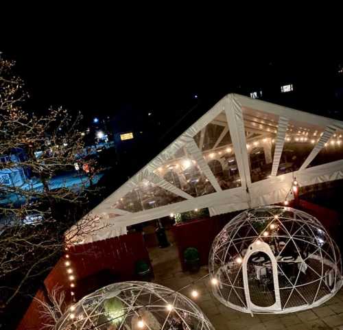 A cozy outdoor dining area with illuminated geodesic domes and string lights, set against a night sky.