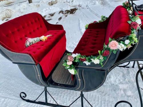 A festive red velvet sleigh decorated with flowers, set against a snowy background.