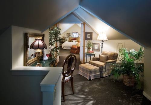 Cozy attic space with a chair, lamp, and plants, leading to a bedroom in the background. Warm, inviting atmosphere.