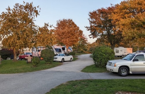 A scenic RV park with autumn trees, parked RVs, and a white car on a winding path.