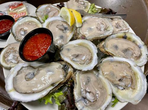 A platter of fresh oysters on a bed of lettuce, served with lemon wedges and two bowls of cocktail sauce.