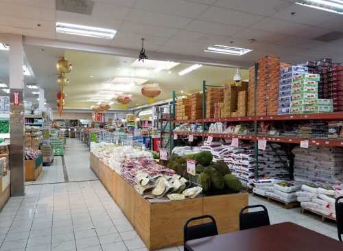 A spacious grocery store aisle filled with various food products, including rice, snacks, and fresh produce.