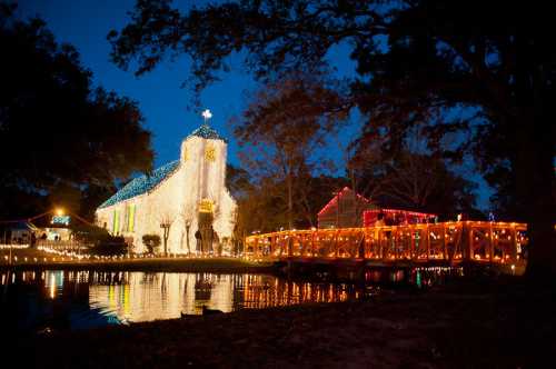 A beautifully lit church and bridge at night, reflecting in the water, surrounded by festive decorations.