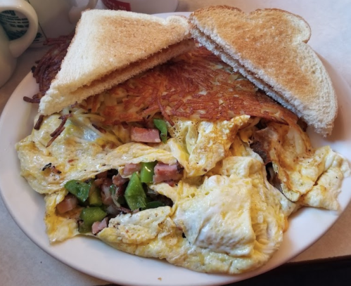 A plate of omelette with green peppers and ham, served with crispy hash browns and two slices of toast.