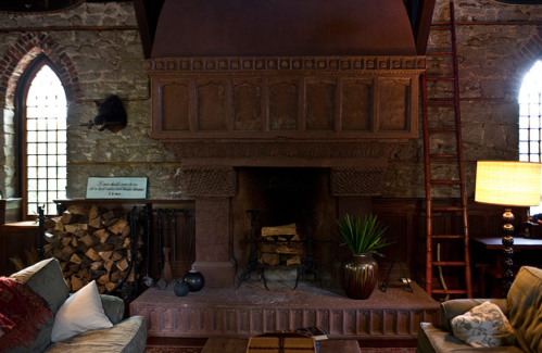 Cozy interior featuring a large stone fireplace, wooden accents, a stack of firewood, and a warm lamp.