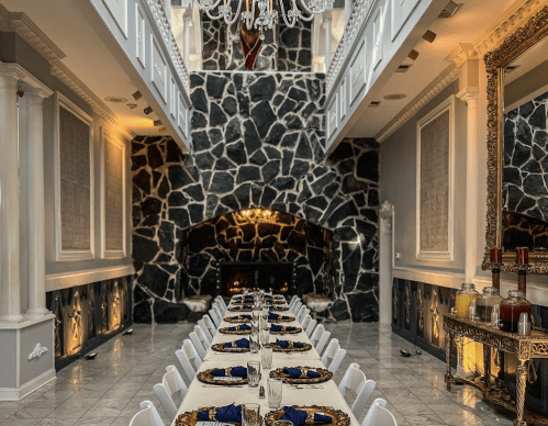 Elegant dining room with a long table set for a formal meal, featuring stone walls and a grand chandelier.