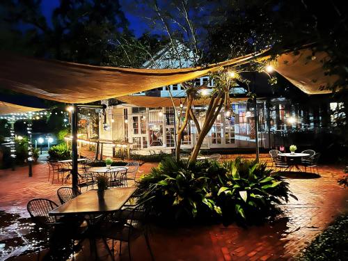 A cozy outdoor dining area with string lights, shaded tables, and lush greenery at night.