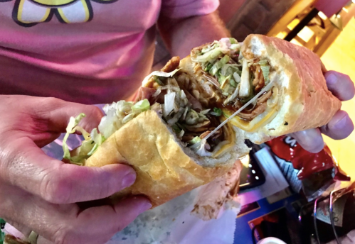 A person holds a large sandwich filled with shredded meat, lettuce, and cheese, revealing its contents.