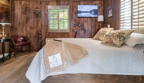 Cozy bedroom with wooden walls, a large bed, decorative pillows, and a TV, featuring a welcoming blanket on the bed.