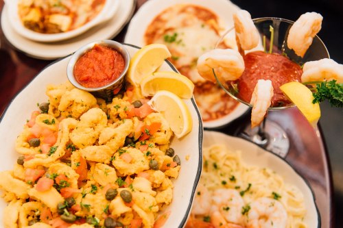 A variety of seafood dishes, including shrimp cocktail, pasta, and a platter of shrimp with lemon and marinara sauce.