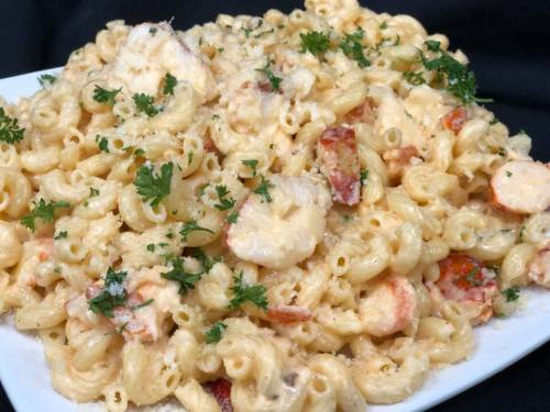Creamy macaroni and cheese with shrimp and lobster, garnished with fresh parsley on a white platter.