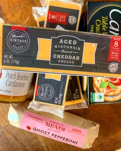 A selection of gourmet cheeses and meats, including aged cheddar and ghost pepperoni, arranged on a wooden surface.