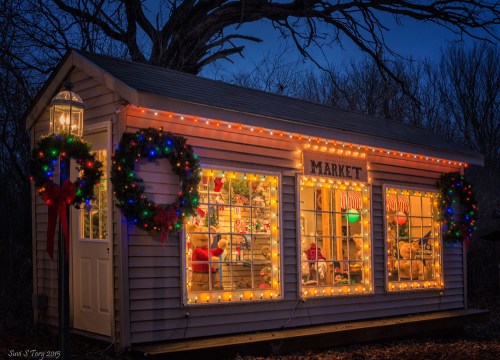 A cozy market building adorned with festive lights and wreaths, glowing warmly in the evening.