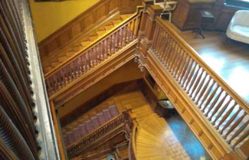 A wooden staircase with ornate railings, viewed from above, leading to a lower level in a well-lit interior.