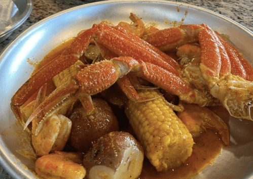 A bowl of seafood featuring crabs, shrimp, corn, and potatoes in a spicy sauce.