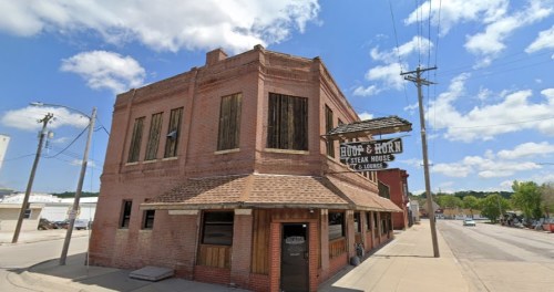 Exterior view of the HooP & Horn Steak House, a brick building with a sign, under a blue sky with clouds.